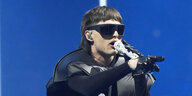 Peso Bluma mit schwarzen Handschuhen und Sonnenbrille hält ein Mikrofon