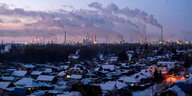 Vögel fliegen über Gebäude der Stadt Omsk, im Hintergrund steigt Rauchgas und Dampf aus Schornsteinen einer Ölraffinerie