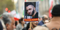 Ein Demonstrierender hält ein Schild mit dem Portät vom Papper Toomaj Salehi in die Höhe.